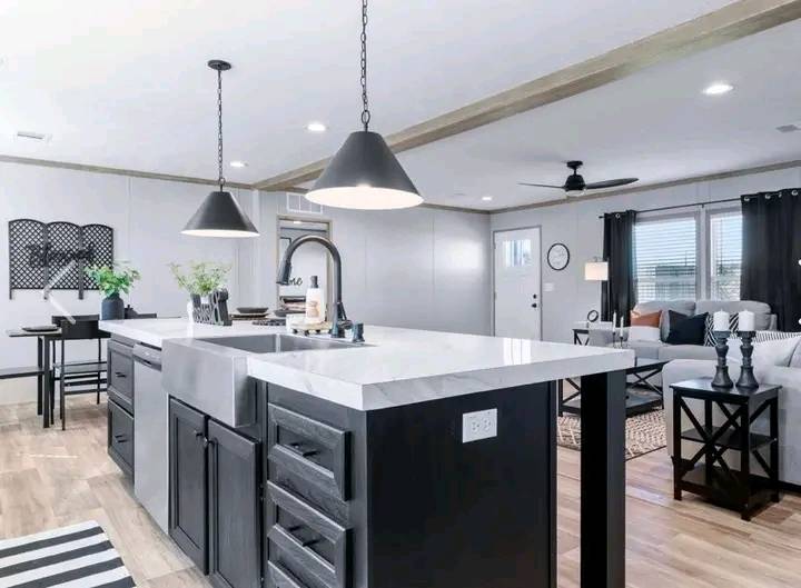 Modern kitchen and living area featuring a marble-topped island, black pendant lights, and sleek black cabinets. Cozy sofa and curtains in the background.
