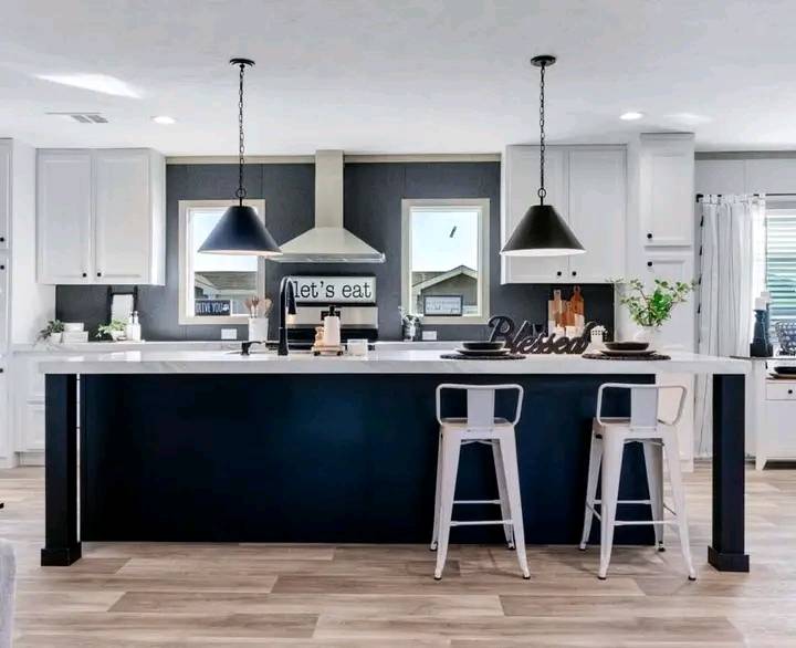 Modern kitchen with a sleek white island, black stools, and pendant lights. A sign reads "let's eat" near the stove, creating a cozy ambiance.