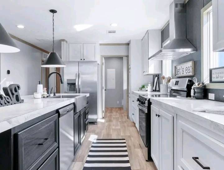 Modern kitchen with black and white decor, featuring a large island, stainless steel appliances, striped rug, and "Let's eat" sign on the wall.