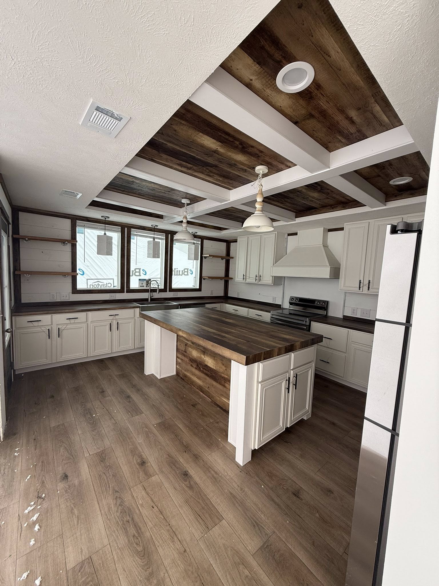 Modern kitchen with rustic elements, featuring white cabinets, wood countertops, a central island, exposed shelves, and wood-paneled ceiling and floor.