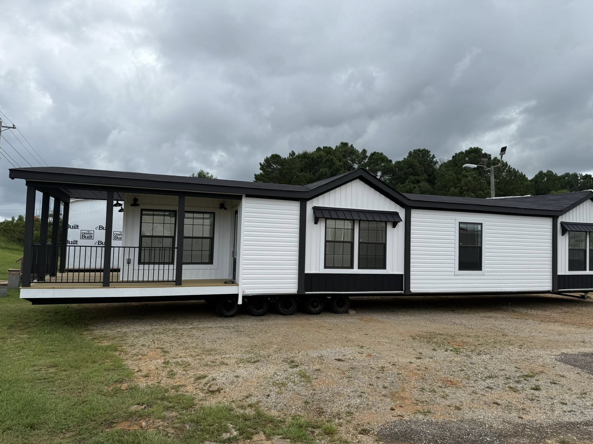 Black and white mobile home with a small porch under a cloudy sky. Surrounded by trees, the scene conveys a calm, rural atmosphere.
