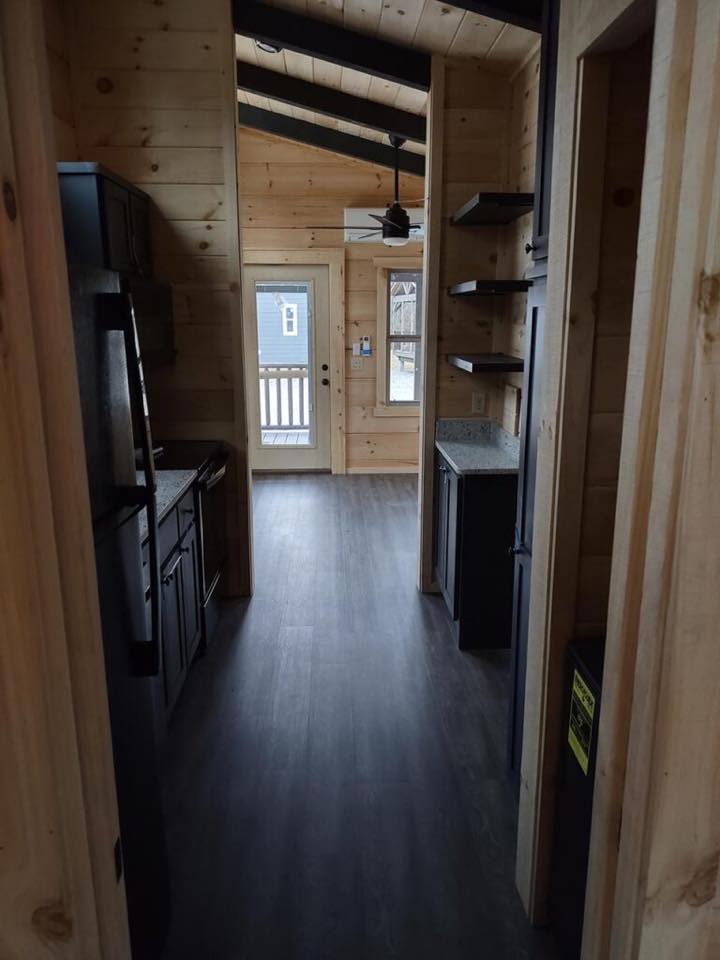 Narrow wooden kitchen with a vaulted ceiling, dark cabinets, and modern appliances. A glass door at the end leads to a porch with a calm, rustic feel.