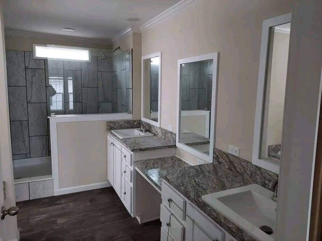 Modern bathroom featuring a granite countertop with dual sinks and white cabinetry. A glass-enclosed shower with large tiles is visible in the background.