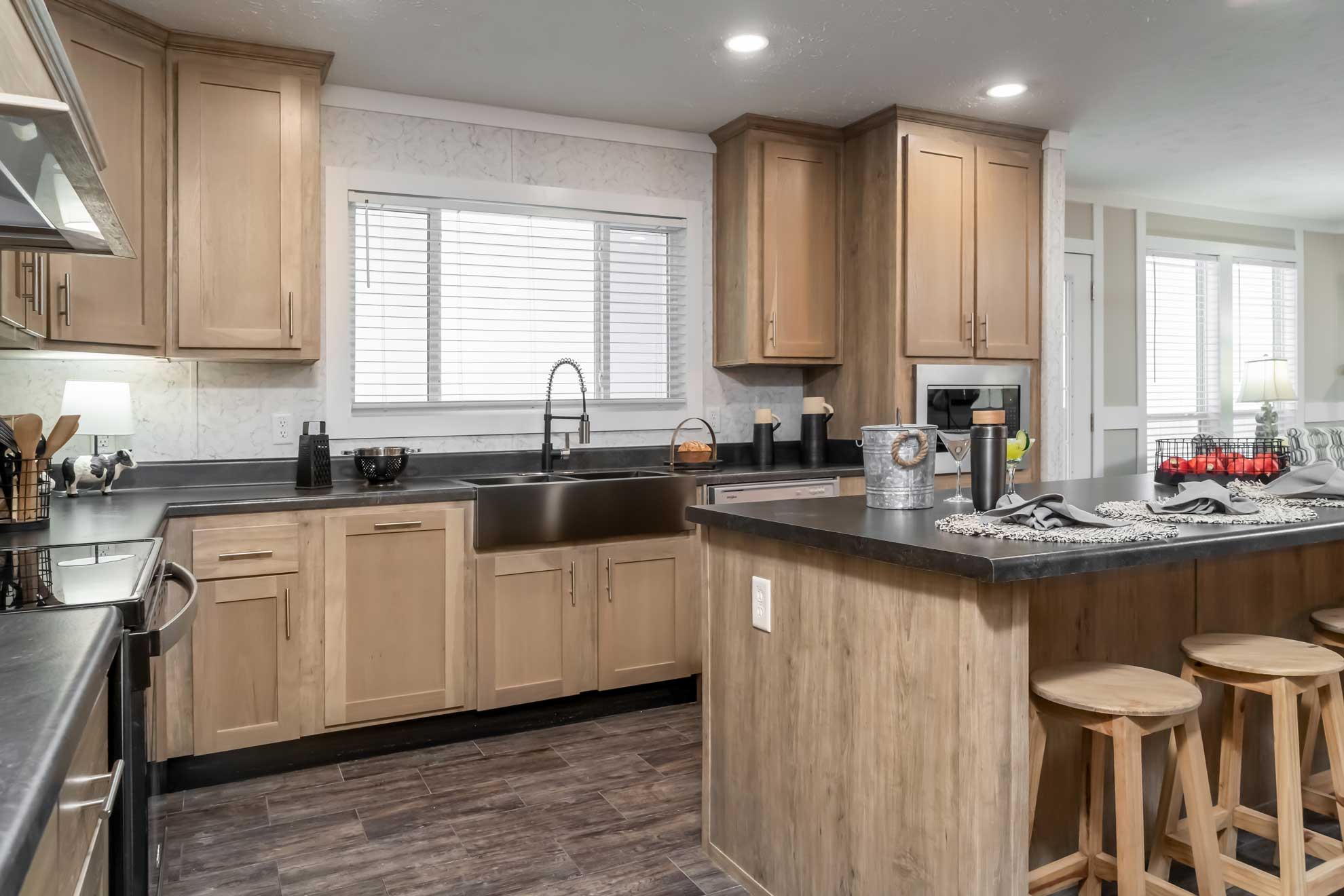 Modern kitchen with wooden cabinets and dark countertops. An island with stools is set for breakfast. Soft lighting and a cozy, inviting ambiance.