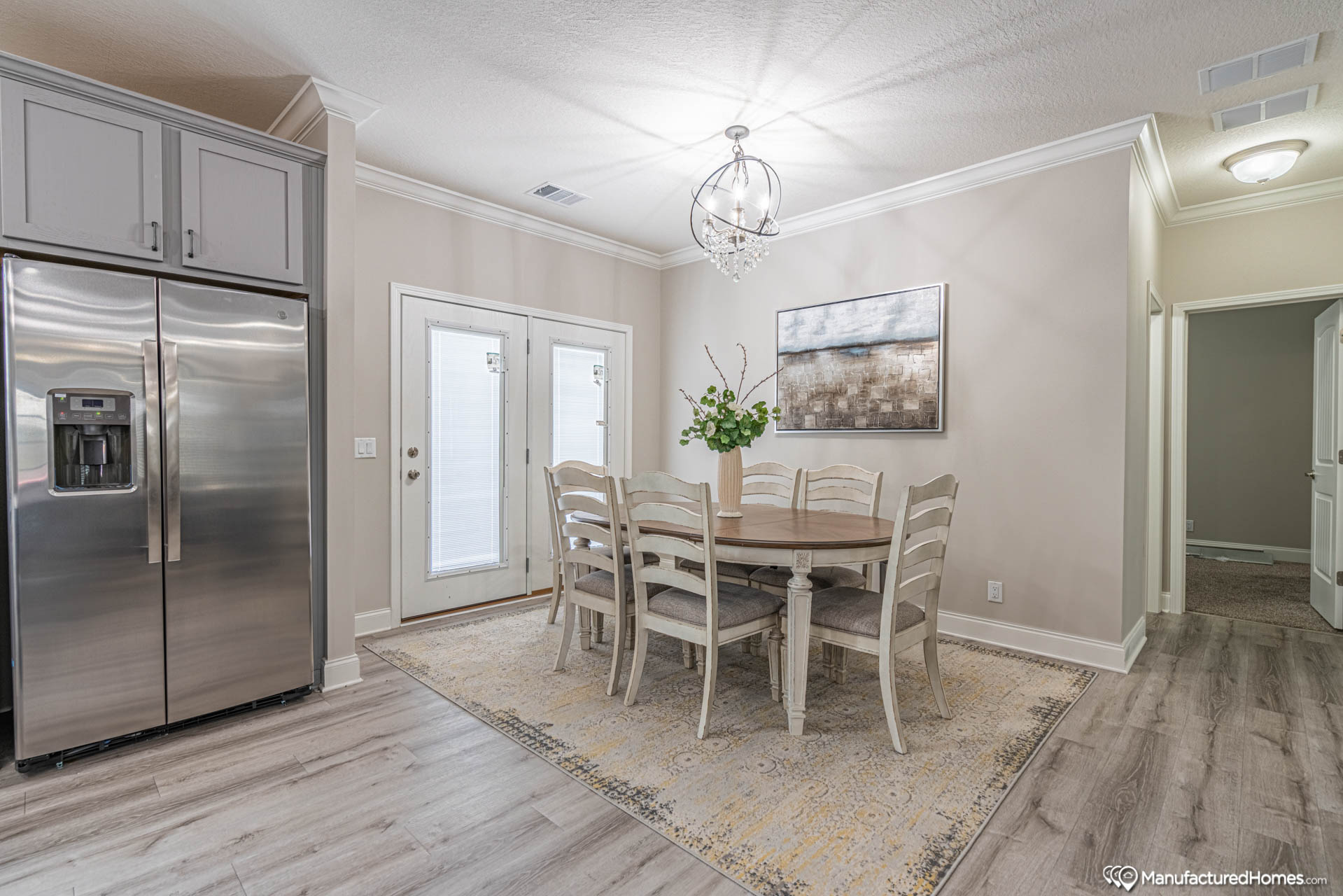 Elegant dining area with a wooden table, six chairs, and a decorative plant under a modern chandelier. Nearby are French doors and a stainless steel fridge.