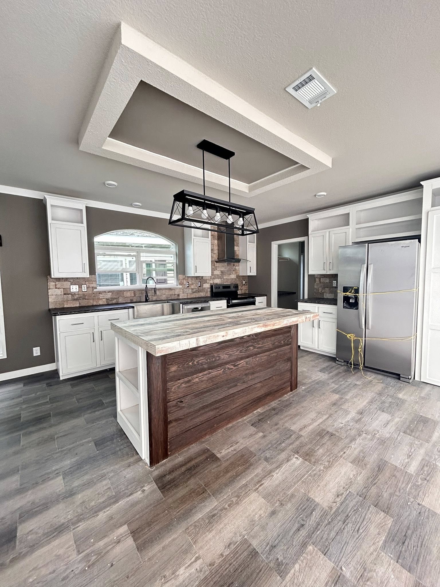 Spacious kitchen with a rustic island, modern lighting, and stainless steel appliances. Neutral tones and wood flooring create a warm, inviting atmosphere.