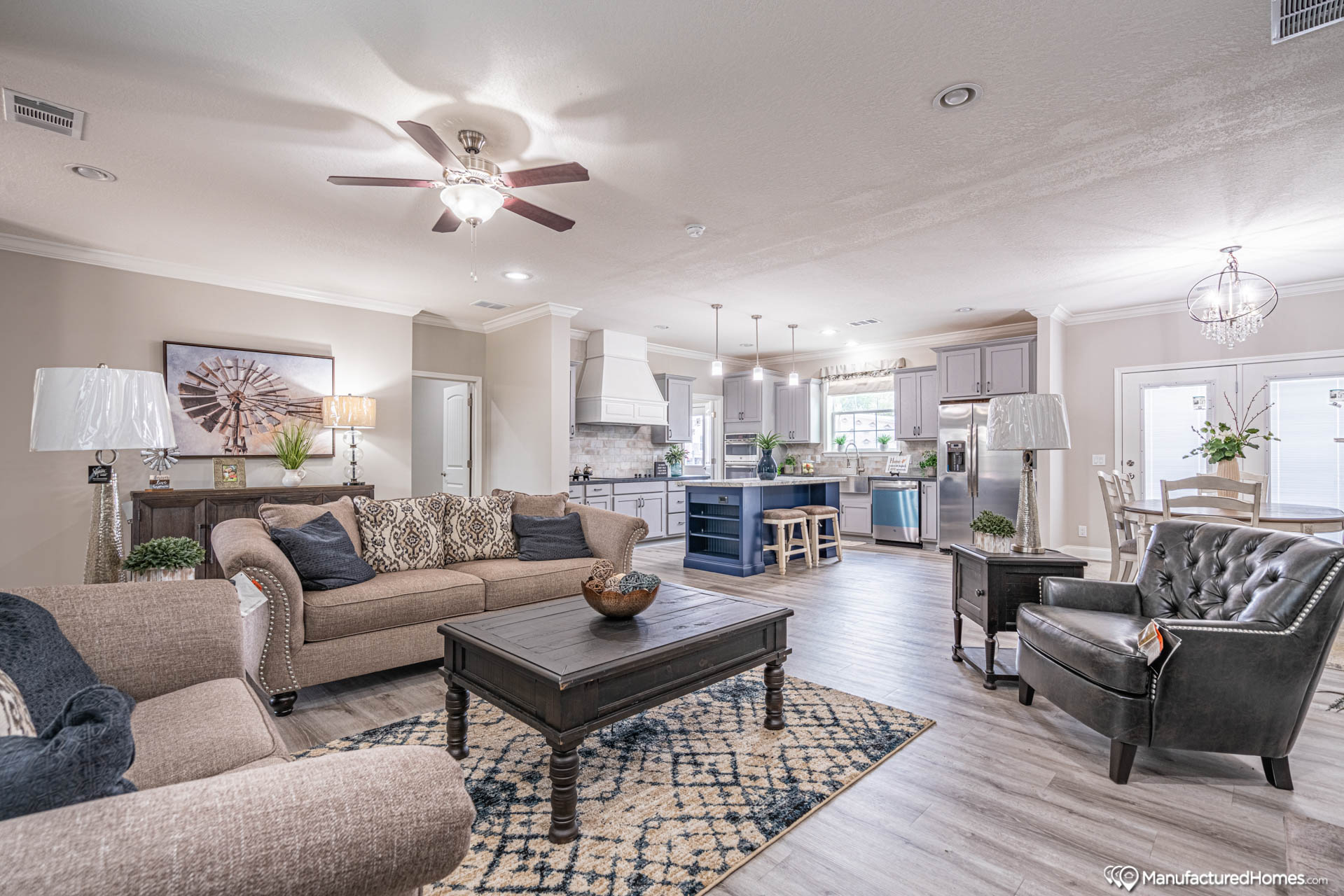 Spacious living room and kitchen with cozy gray sofas, a patterned rug, and modern decor. Bright and inviting with ample natural light.
