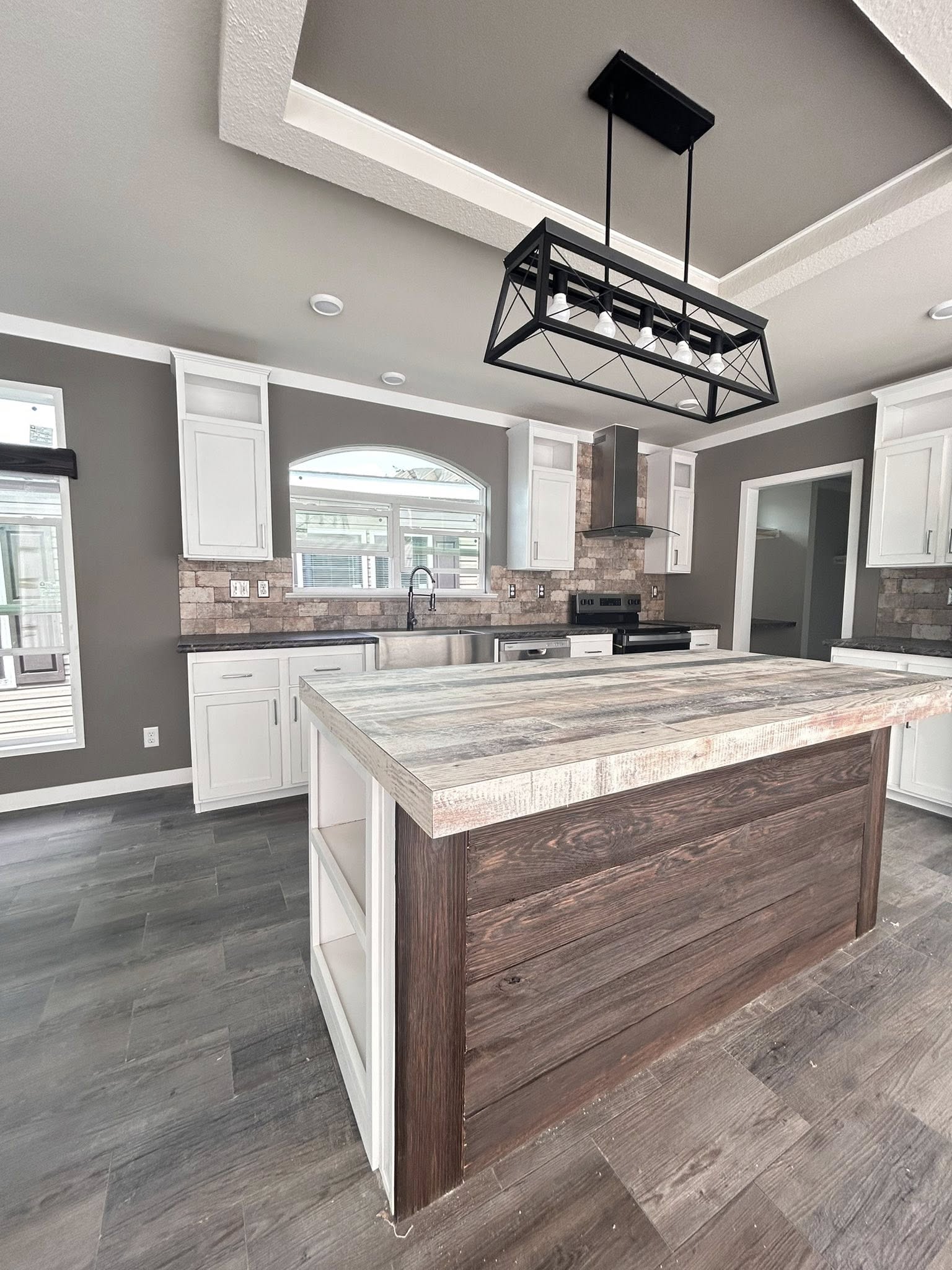 Modern kitchen with gray and white tones, featuring a central wooden island, industrial black light fixture, stainless steel appliances, and sleek cabinetry.