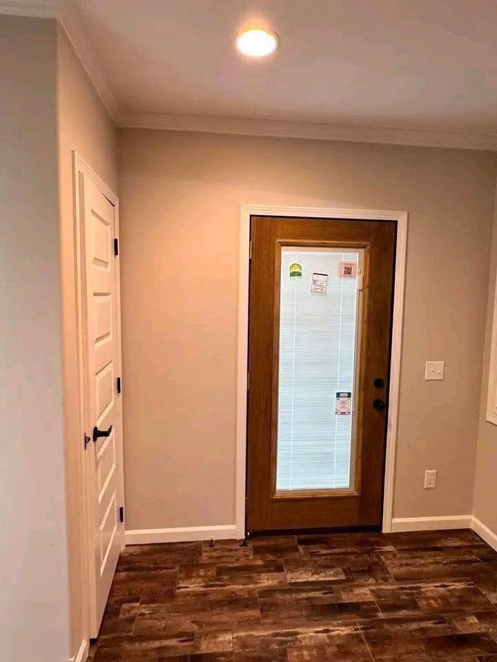 Modern entryway with wood-textured flooring, a wooden door with glass panes, white walls, and a ceiling light casting a warm glow. Cozy and inviting.