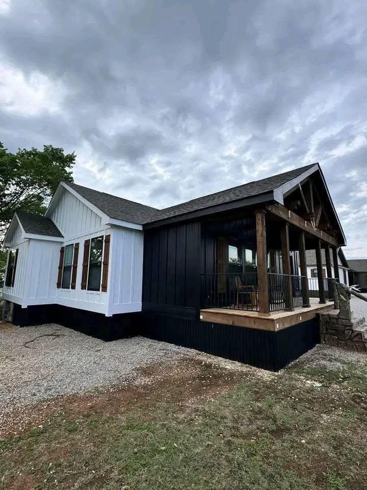Modern house with black and white exterior, wooden accents, and a front porch under a cloudy sky. The scene conveys a cozy, rustic charm.