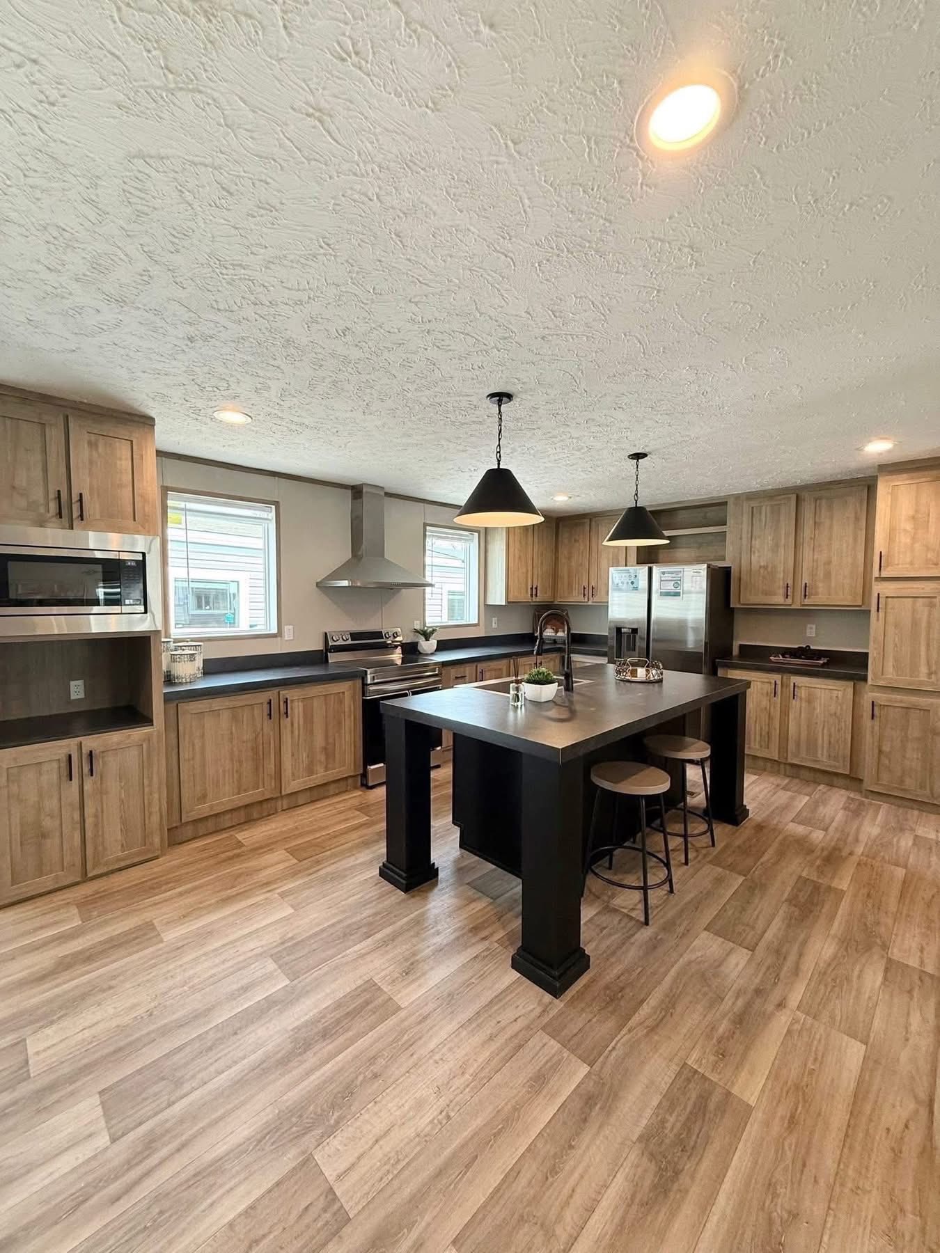 Modern kitchen with wood cabinets, dark countertops, and a sleek island with barstools. Pendant lights hang above. Bright, welcoming ambiance.