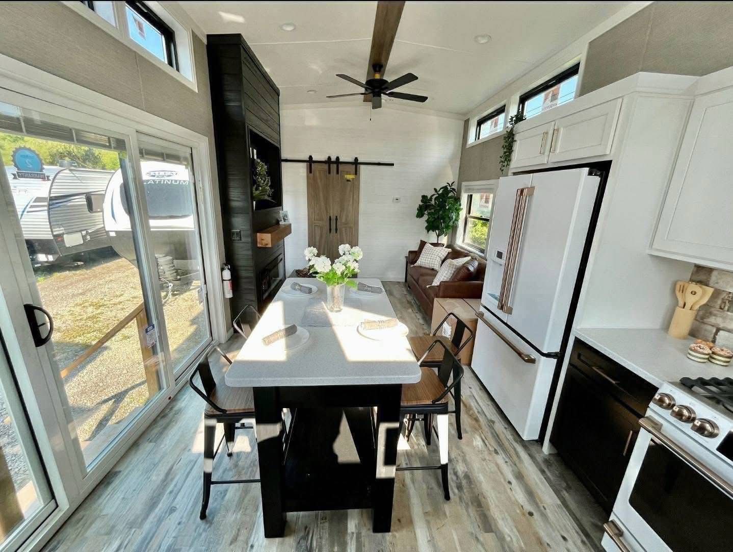 Modern RV interior with a spacious kitchen and living area. Features a central island with chairs, white cabinetry, and a cozy couch, creating an inviting, open atmosphere.