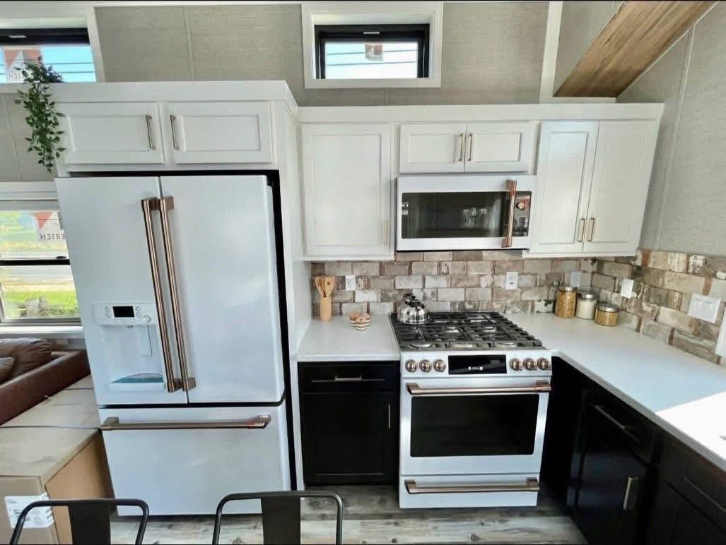 Modern kitchen with white cabinets, stone backsplash, and black lower cabinets. Features stainless steel appliances and wooden accents, creating a cozy, inviting space.