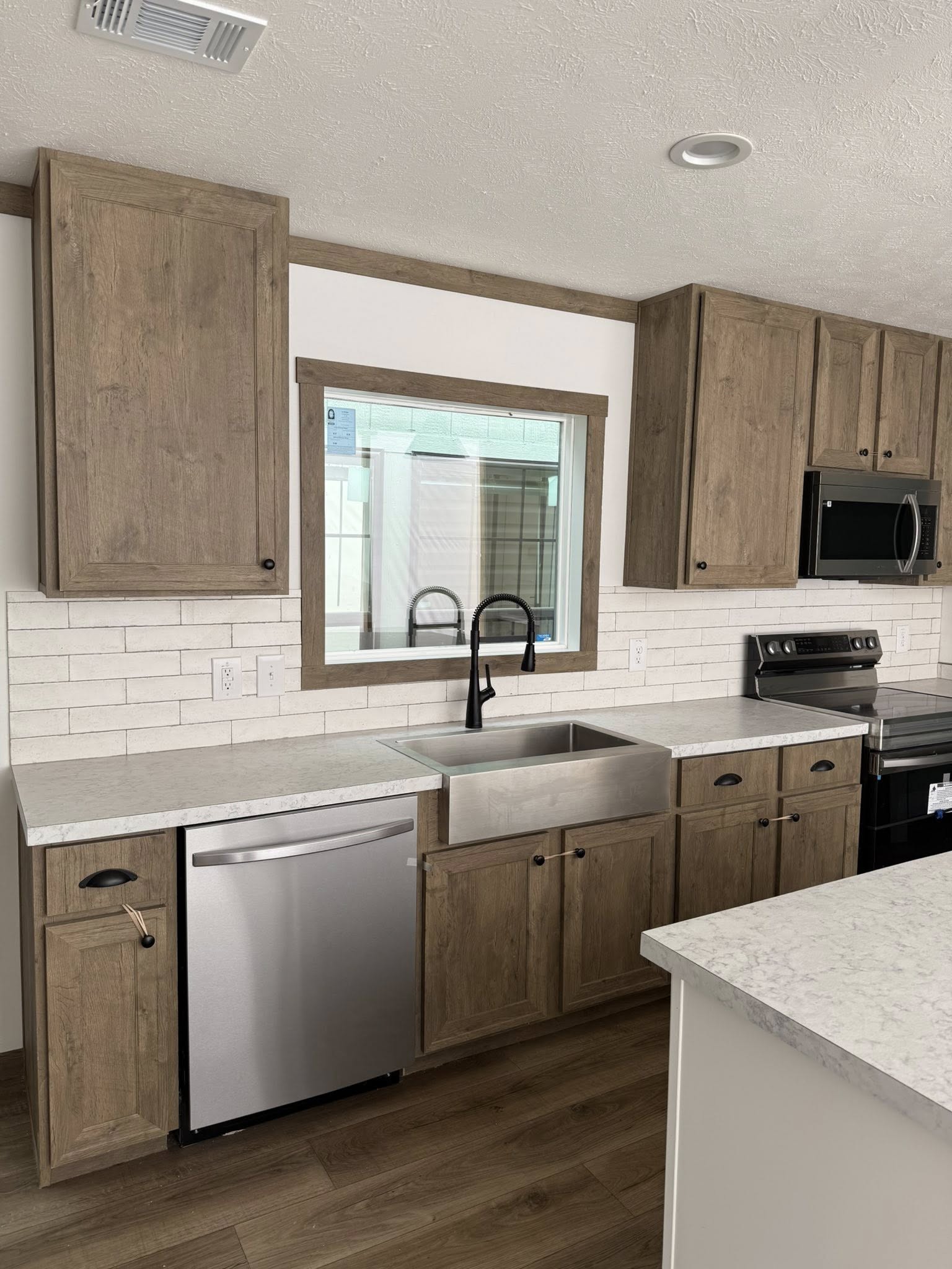 A modern kitchen with rustic wooden cabinets, a stainless steel dishwasher, and a sleek black faucet over a large sink. Light brick backsplash adds brightness.