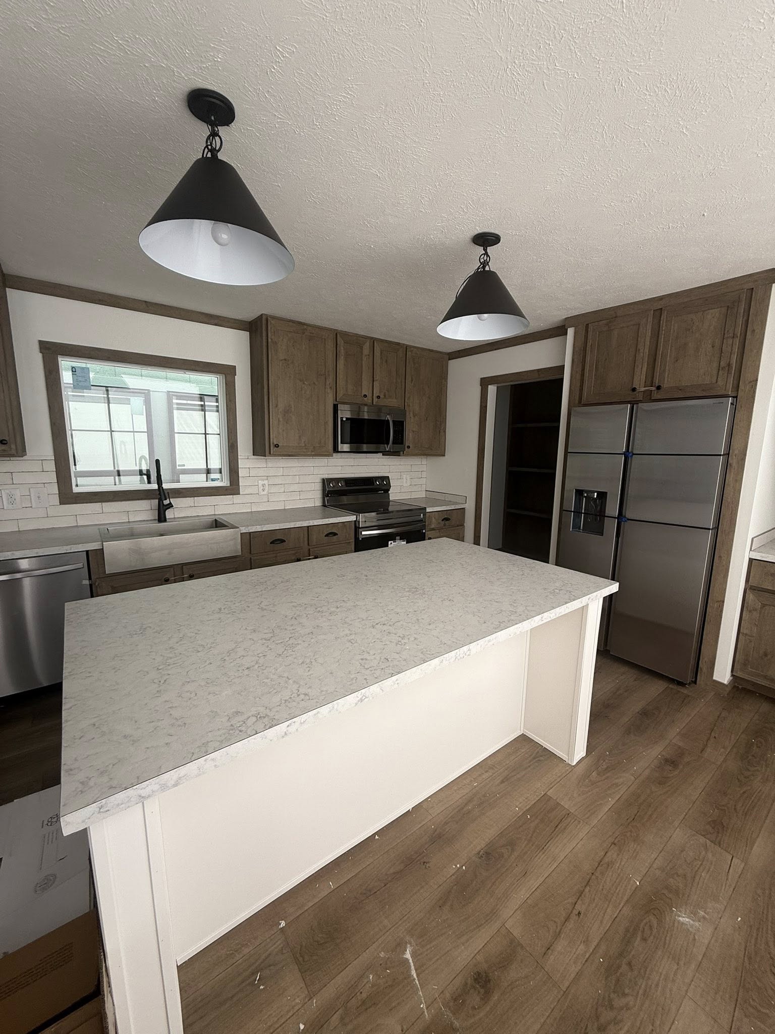 Modern kitchen with a white island countertop, wooden cabinets, stainless steel appliances, and pendant lights. Bright and organized atmosphere.