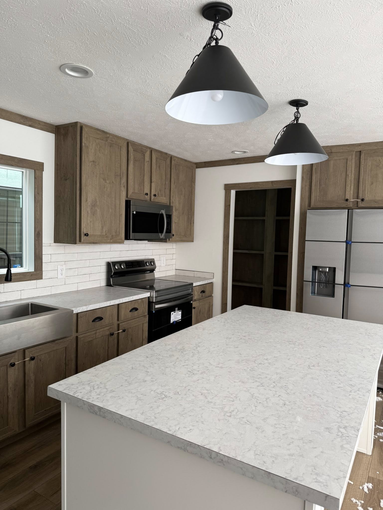Modern kitchen with light wood cabinets, white countertops, and stainless steel appliances. Large island under black pendant lights, cozy ambiance.