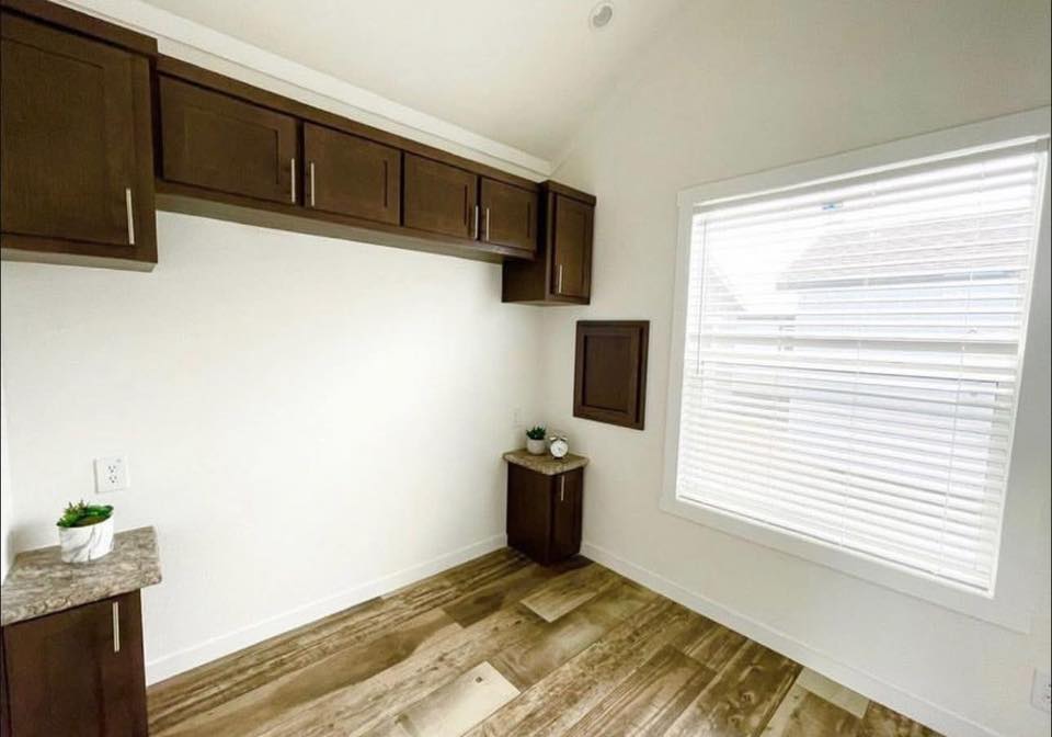Minimalist corner of a room with wood floors, brown cabinets, small side tables, and large blinds on the window. Soft, bright, and uncluttered atmosphere.