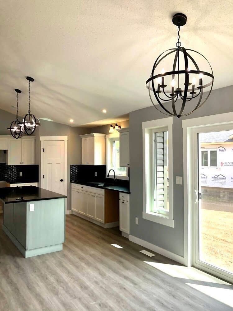 Modern kitchen with gray walls, light wood flooring, black countertops, and white cabinets. Two orb chandeliers hang above the island. Bright and inviting atmosphere.