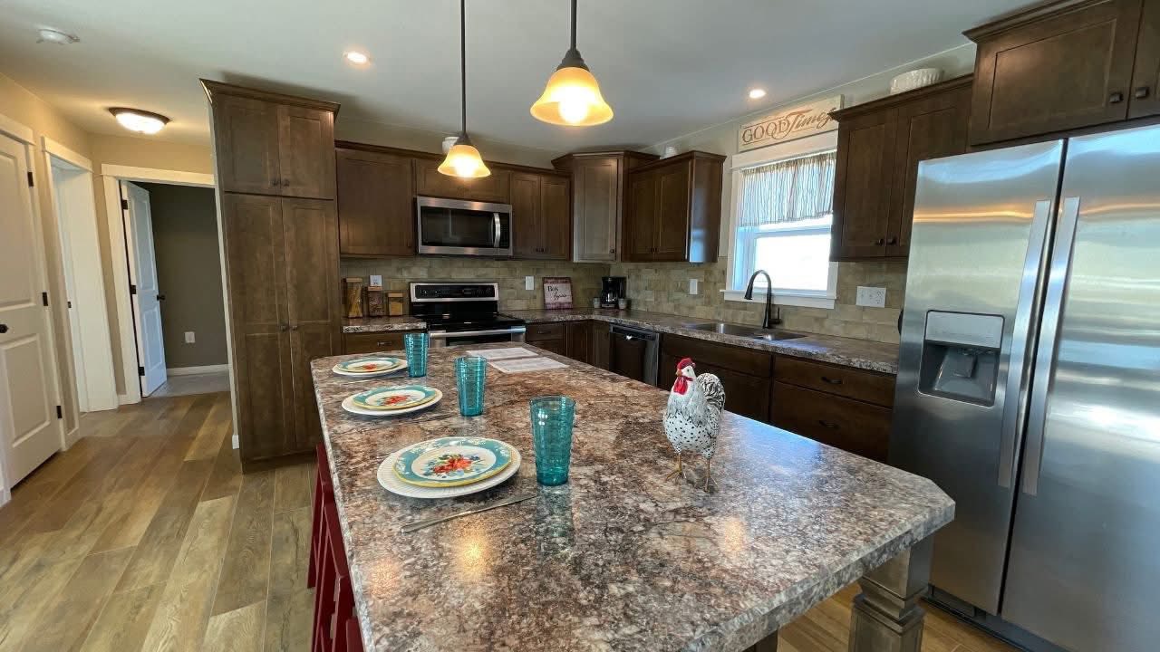 A modern kitchen with warm tones features a marble island set with colorful plates and blue glasses. Soft pendant lights and wood cabinets add a cozy touch.