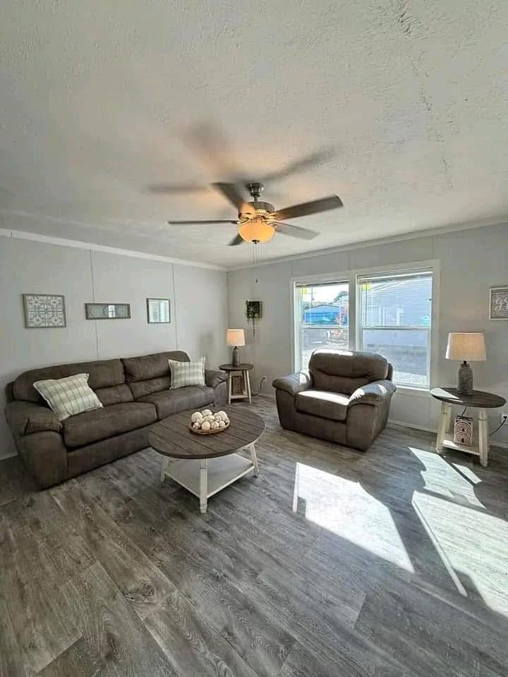 Cozy living room with brown sofas, a coffee table, and wooden flooring. Soft lighting from lamps and sunlight through large windows creates a warm ambiance.