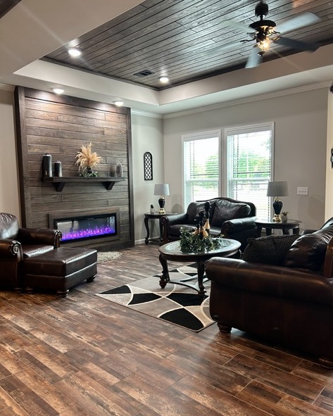 Stylish living room with dark leather sofas, a geometric rug, and a modern fireplace with purple flames. Warm wood flooring and cozy ambiance.