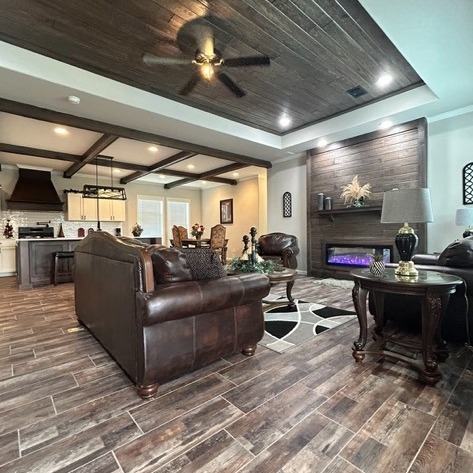 Sophisticated living room with brown leather sofas, wooden floor, ceiling fan, and fireplace. Modern open kitchen in the background. Cozy ambiance.
