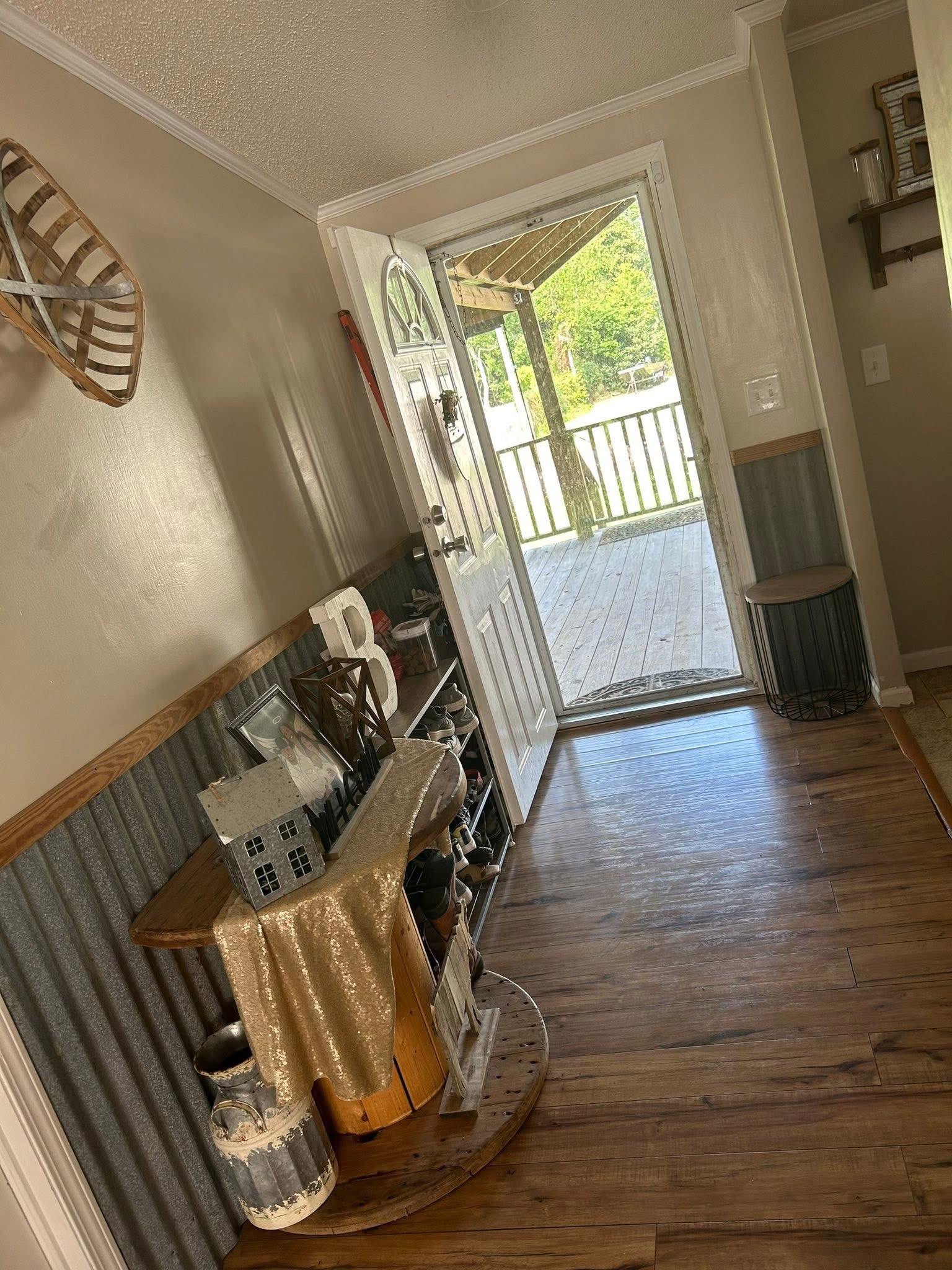 Hallway with wood flooring and open door leading to a porch. Decor includes a gold cloth-covered table with rustic items and a wall snowshoe. Warm, inviting atmosphere.