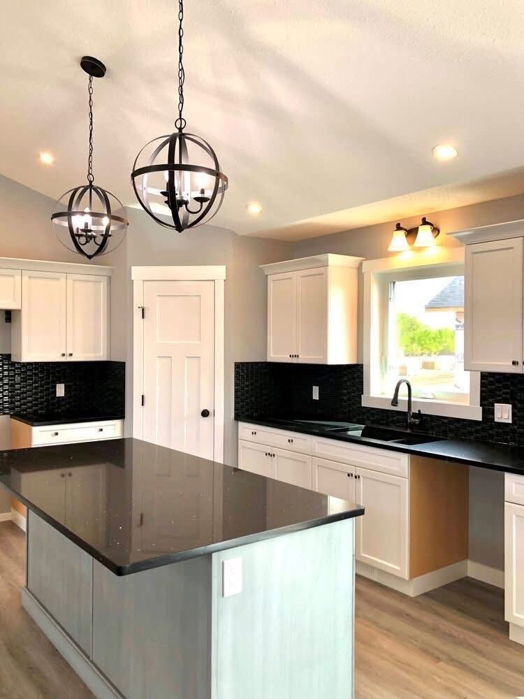 Modern kitchen with a sleek black granite island, white cabinets, and black backsplash. Two spherical pendant lights hang from the ceiling, adding elegance.