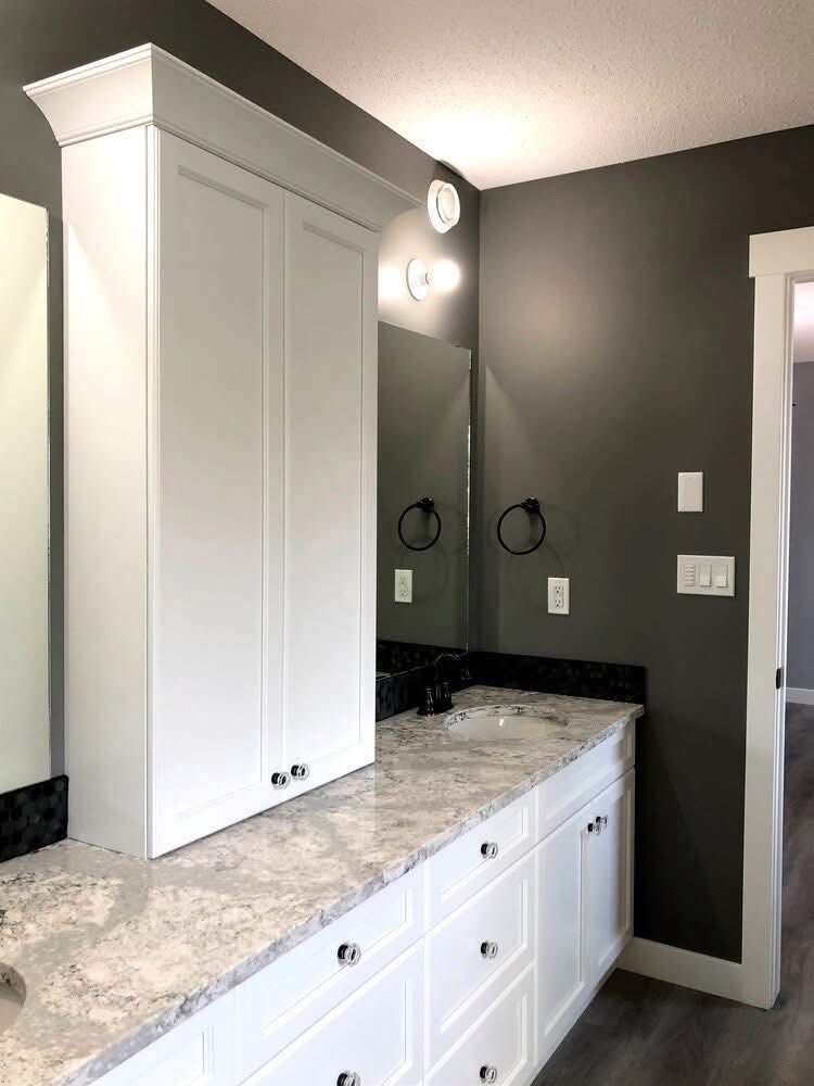 Modern bathroom with white cabinetry and marble countertop. A large mirror is flanked by two circular lights. Gray walls create a sleek, clean ambiance.