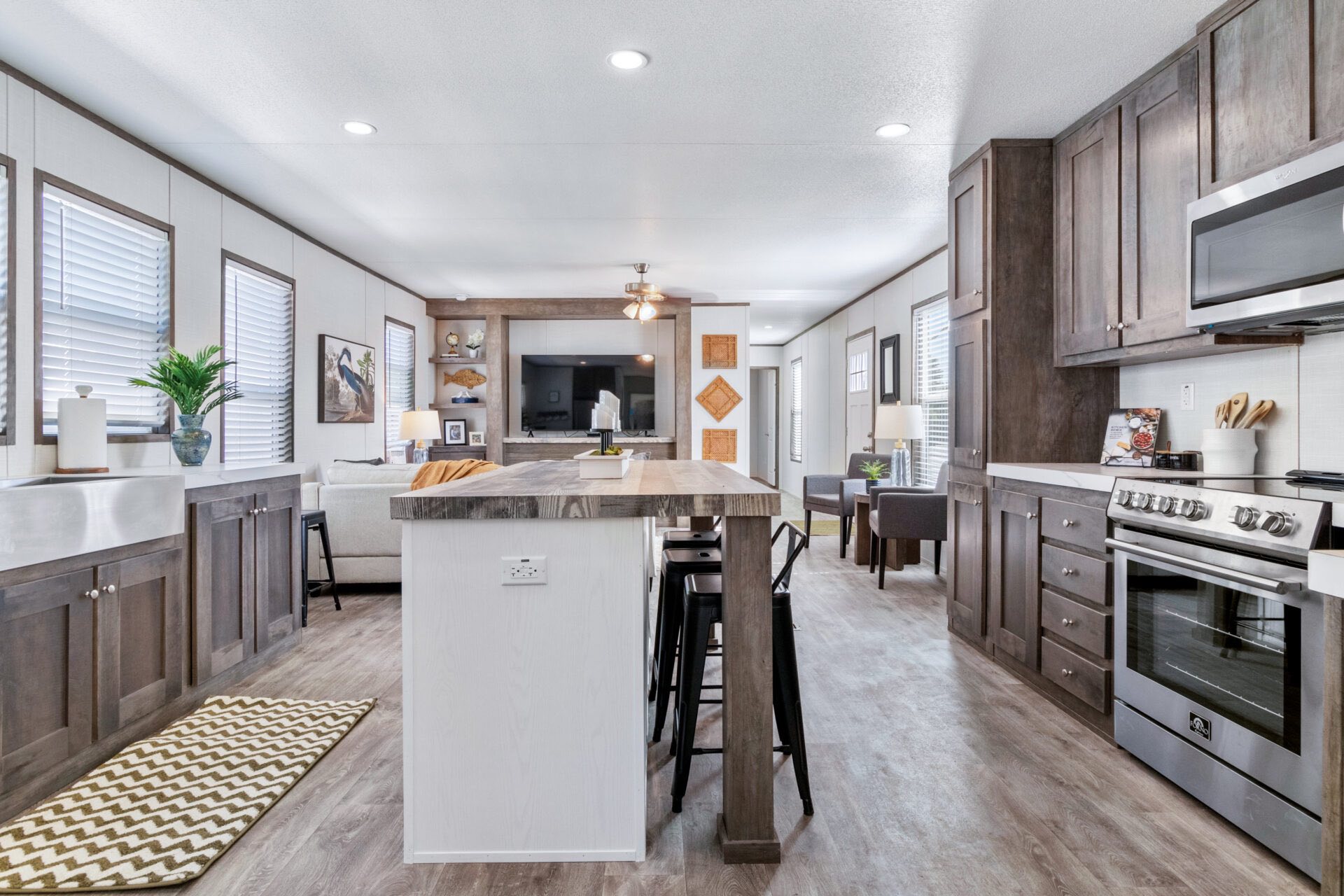 Modern open kitchen and living area with neutral tones. Features wood cabinets, a center island, stainless steel appliances, and a cozy sitting space.