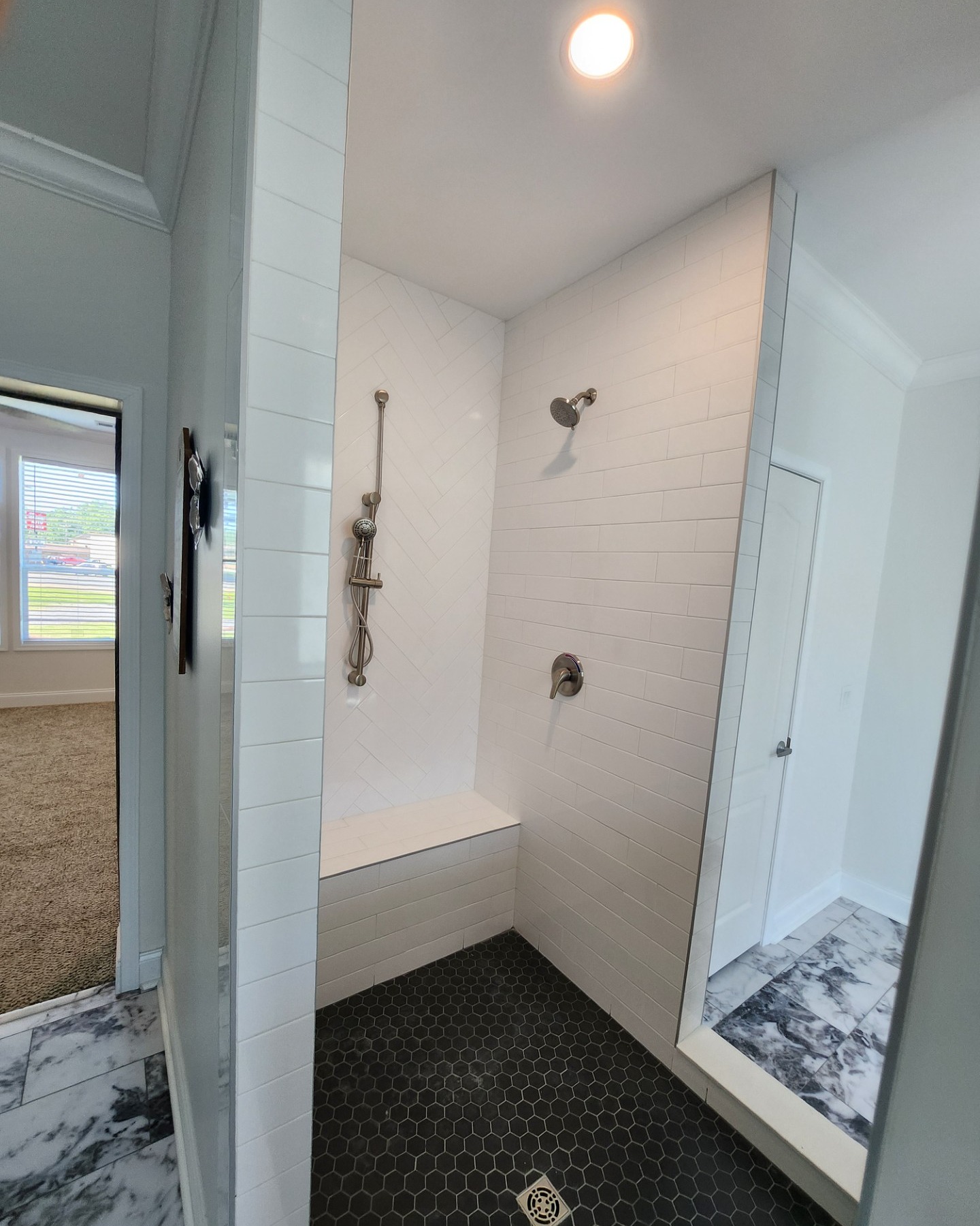 Modern bathroom shower featuring white subway tiles, a bench seat, and a handheld showerhead. The black hexagonal tile floor creates contrast.