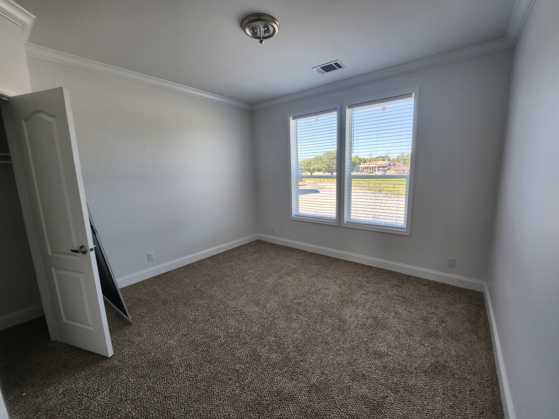 Empty room with beige carpet, white walls, and two large windows letting in natural light. The open closet door is on the left. Minimalistic and bright.