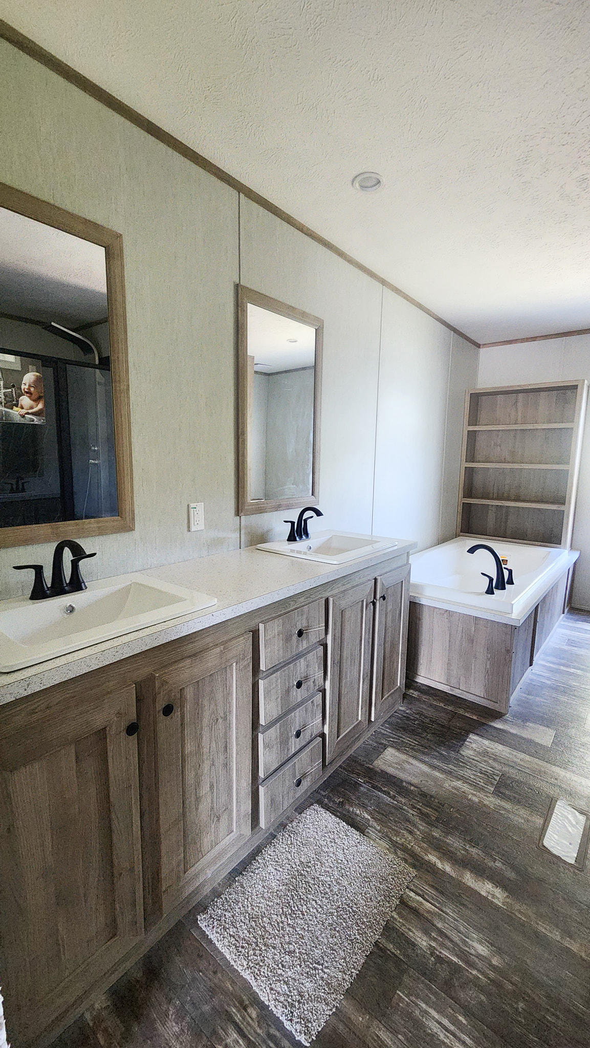 A modern bathroom with dual sinks and black faucets, framed mirrors, a wooden vanity, and a bathtub with an adjacent bookshelf, exuding a clean and elegant vibe.