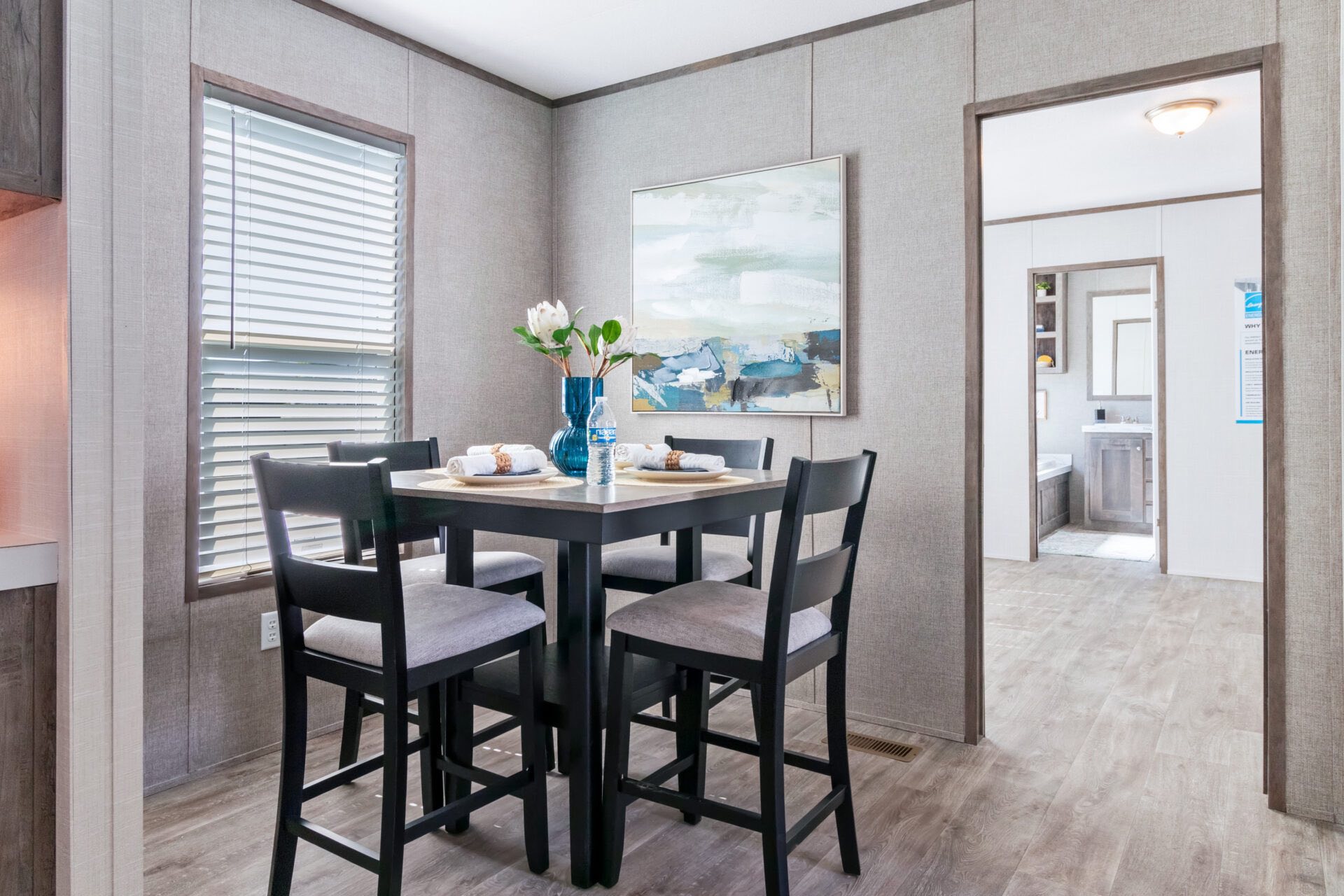 Cozy dining area with a square table set for four, featuring a blue vase with white flowers. Gray tones dominate, evoking a calm, inviting mood.