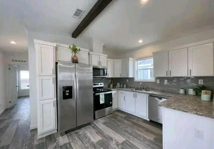 Modern kitchen with white cabinets, stainless steel appliances, and granite countertops. Grey wood flooring and under-cabinet lighting create a sleek, inviting ambiance.