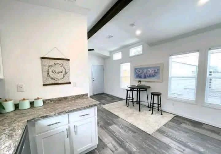 Bright kitchen and dining area with white walls and wood floors. Granite countertop with mint jars, wall art reads "blessed," round table with two stools.