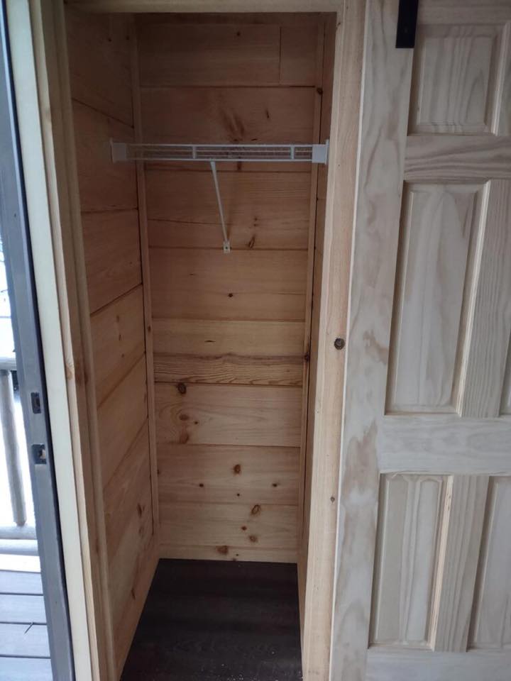 Small, narrow wooden closet with unfinished pine walls and an empty wire shelf. The open door reveals the cozy, rustic interior.