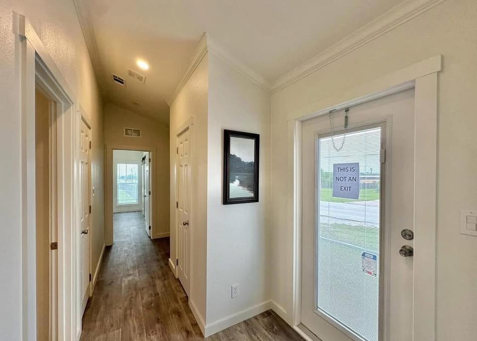 Bright hallway with wood flooring and white walls. A closed door with "This is not an exit" sign is on the right. Two doors line the left wall.