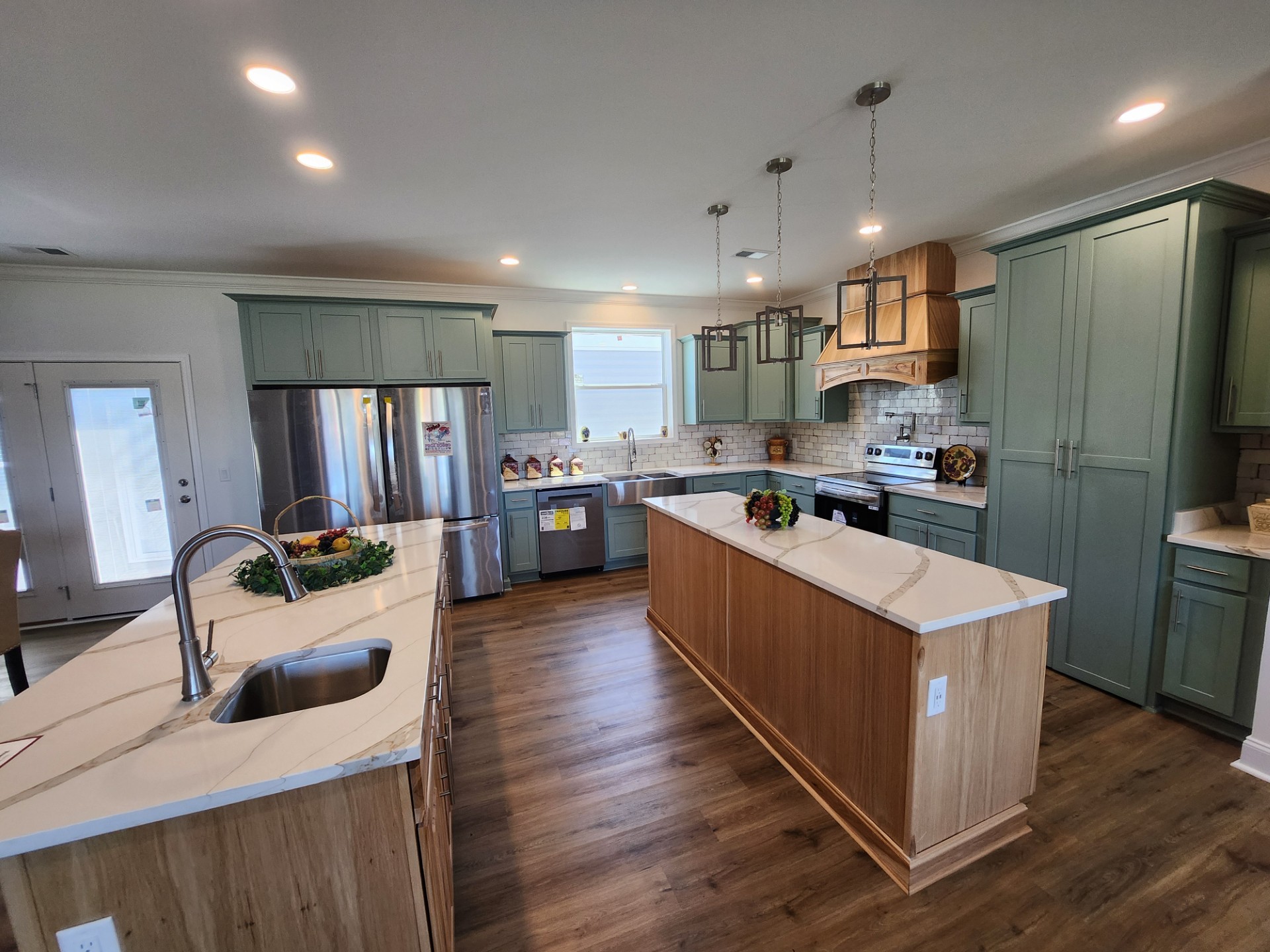 Modern kitchen with wooden floors, a central island, marble countertops, and sage green cabinets. Bright lighting, stainless steel appliances, and a warm, inviting atmosphere.