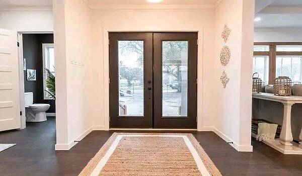 Modern entryway featuring a black double door with glass panels, light walls, dark wood floor, a woven rug, and decorative wall accents. Cozy and inviting.