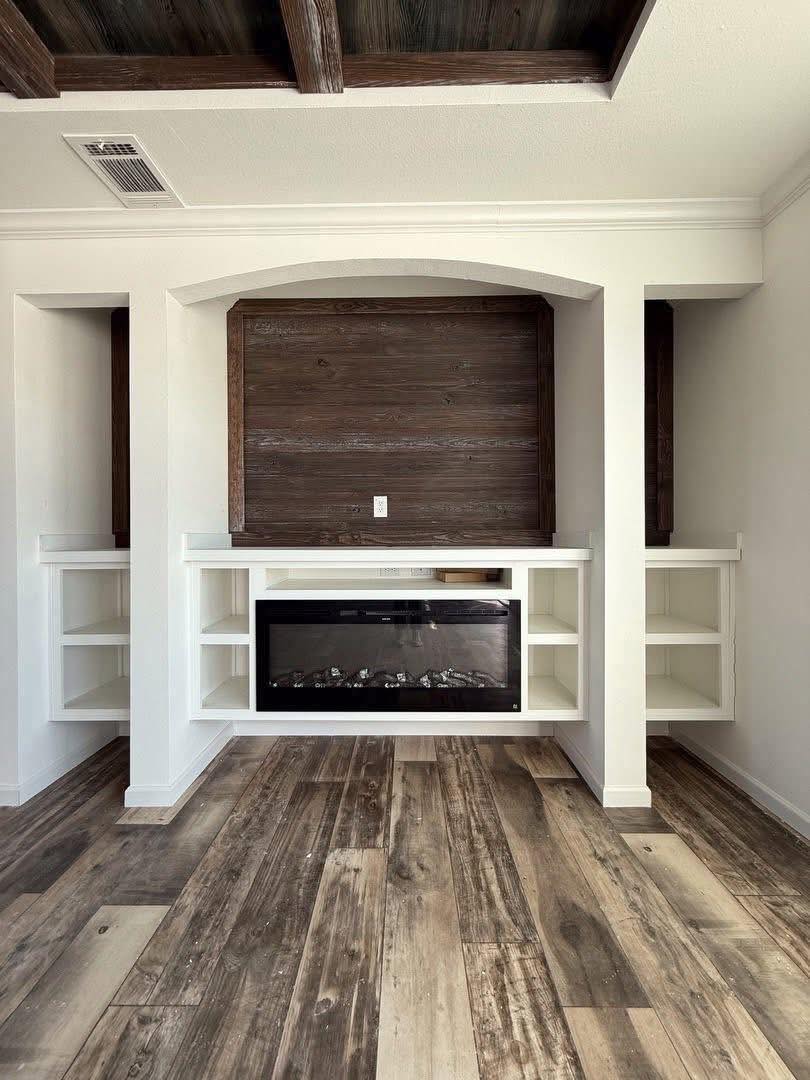 White room with wood accents and rustic flooring. Central recessed space with dark wood backing and shelf niches flanking a black fireplace insert. Cozy and modern.