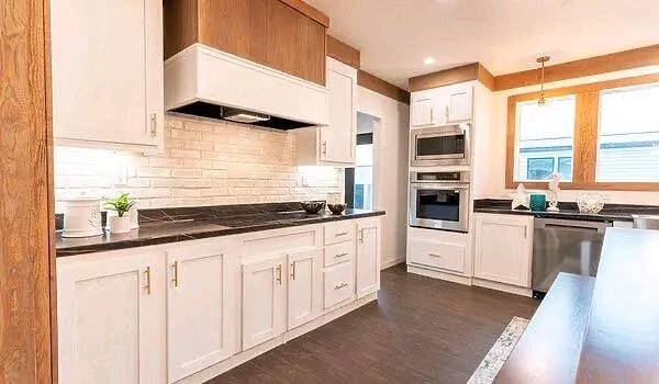 Modern kitchen with white cabinets, dark countertops, and stainless steel appliances. Natural light from a window creates a bright, inviting atmosphere.