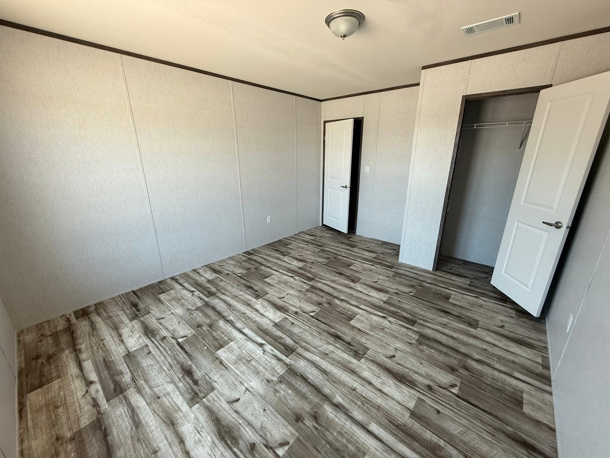 An empty room with light gray walls and wood-patterned laminate flooring. Two white doors, one to a closet, add a clean, minimalist feel.