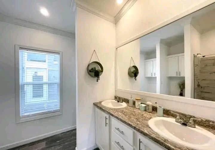 A modern bathroom with a large mirror above a granite double sink vanity. Two hanging round planters add greenery. Soft lighting creates a serene atmosphere.