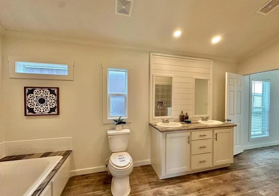 Spacious bathroom with wooden floor, dual-sink vanity, and toilet labeled "Do Not Use." Wall art and plant accentuate the modern decor.