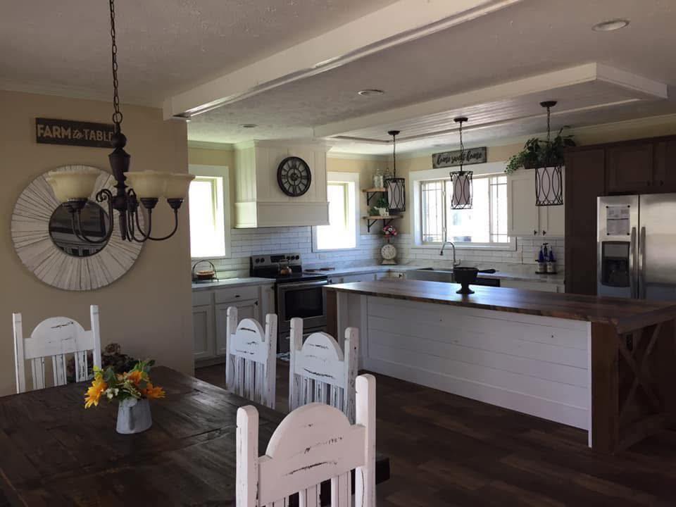 Spacious farmhouse kitchen with white cabinets, a large wooden island, and rustic decor. A dark wood dining table features sunflowers in a vase, under warm lighting.