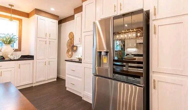 Modern kitchen with white cabinets and a stainless steel refrigerator. Wooden accents and bright lighting create a warm, contemporary feel.