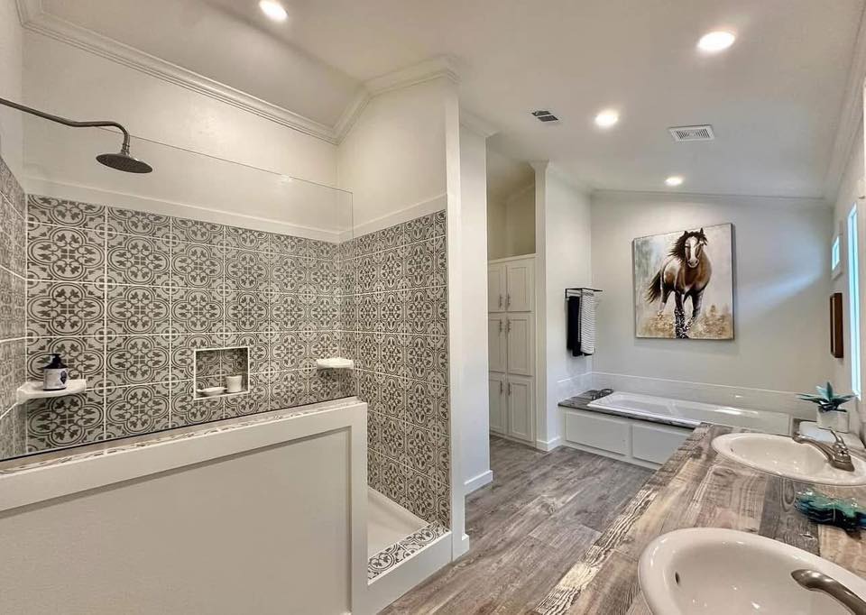 Modern bathroom with wood flooring, dual sinks, and a patterned-tile shower. A bathtub sits below a horse painting, adding a rustic touch.