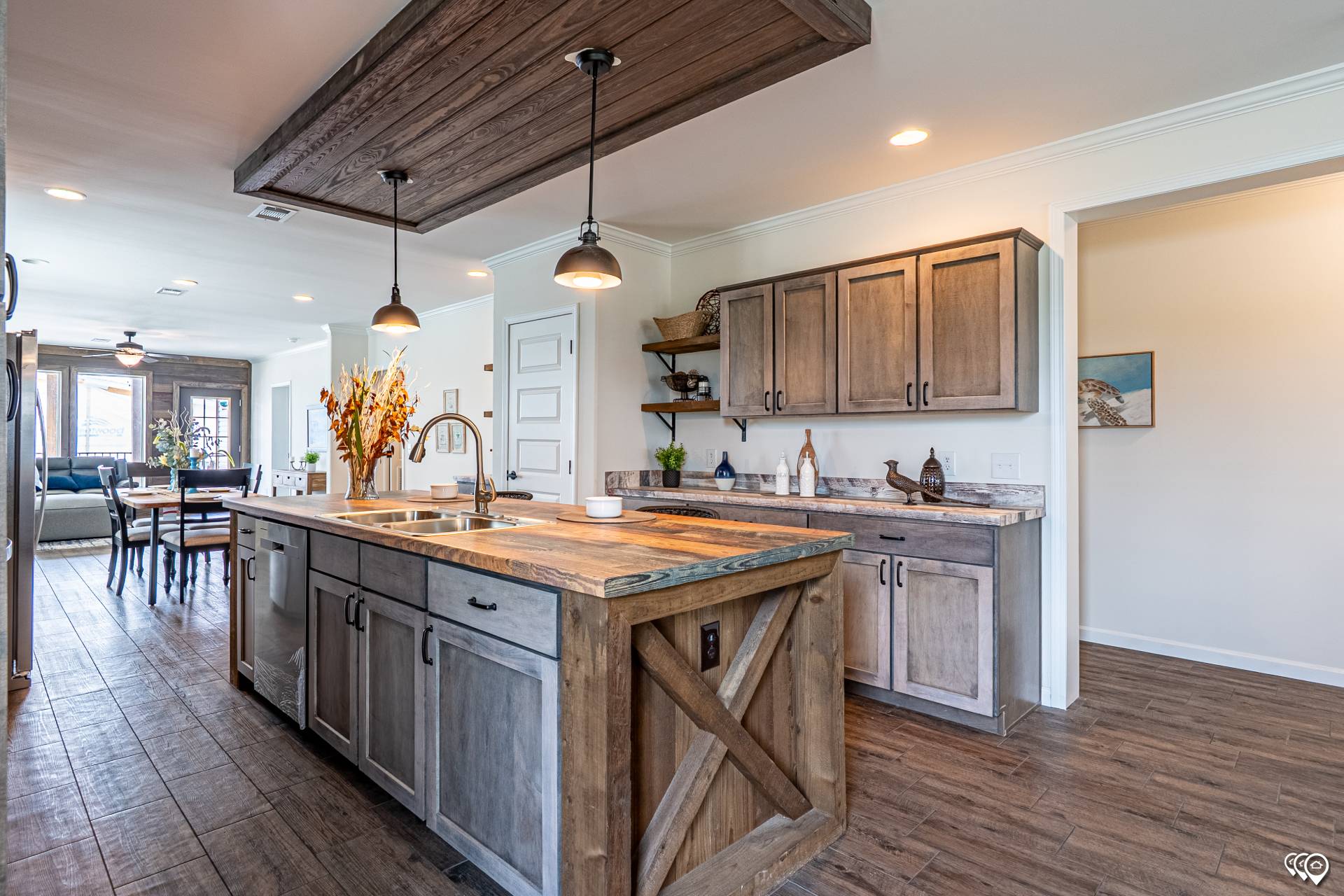 Rustic kitchen with wooden cabinets, a large central island, and pendant lights. Dining area in the background, conveying a warm, inviting atmosphere.