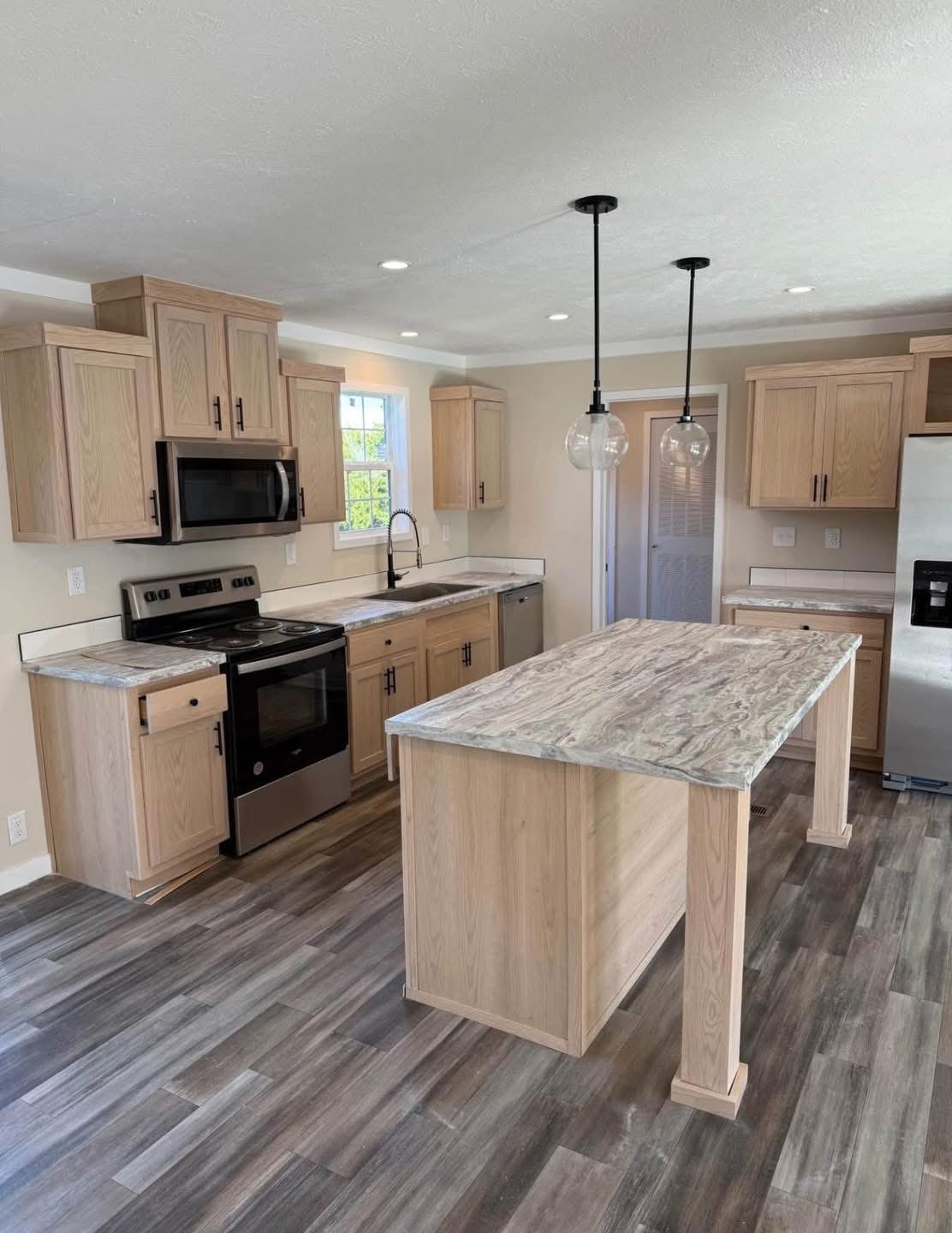 Modern kitchen with wooden cabinets and marble countertops. Features a kitchen island, stainless steel appliances, and pendant lights, exuding a sleek, cozy vibe.